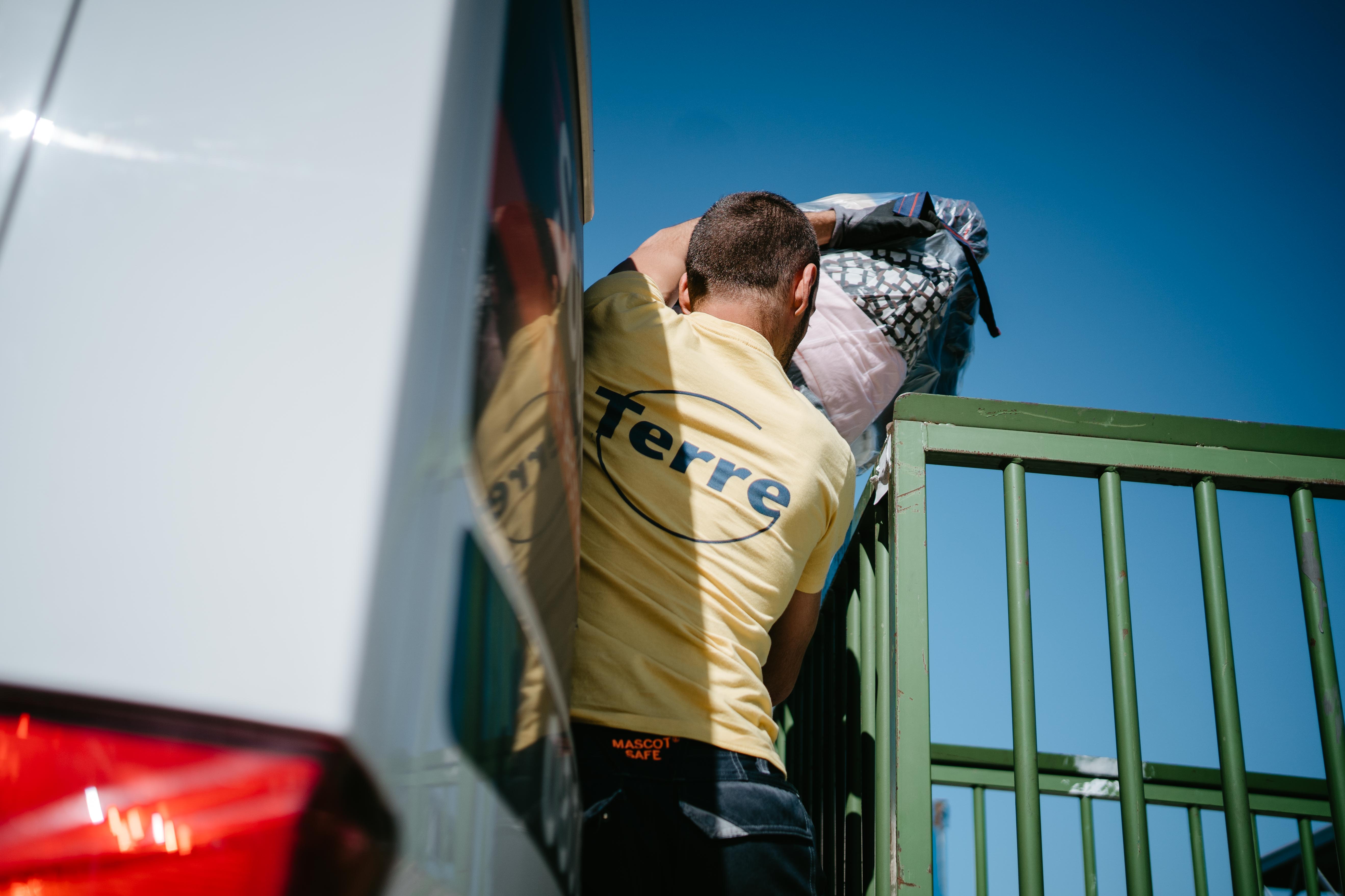 Un homme habillé d'un t-shirt jaune avec le logo Terre jette un sac de textiles dans une camionnette